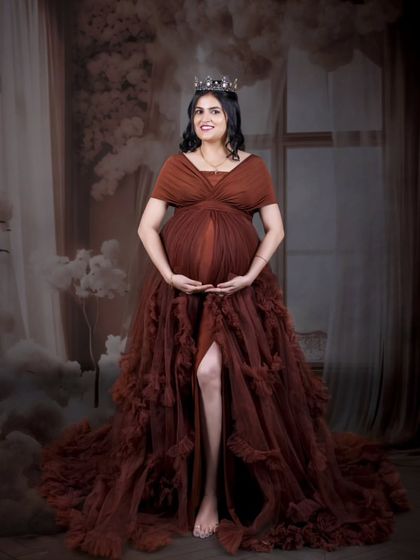 A confident and queenly solo portrait. Wearing a crown and a magnificent brown ruffled gown, the mom-to-be radiates power and grace.
