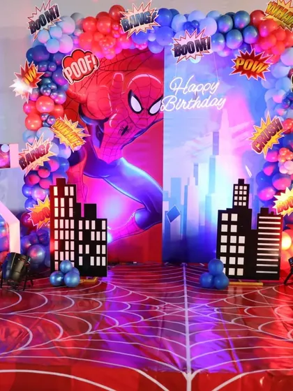 An explosive Spider-Man theme with a "POW!" and "BOOM!" comic book aesthetic. The backdrop features a city skyline and a vibrant red and blue balloon arch.
