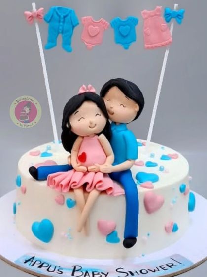 A sweet baby shower cake with a custom figurine of the expecting couple, sitting together under a clothesline of baby items.