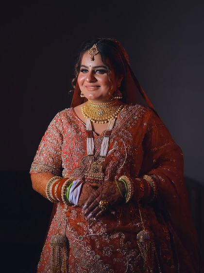 A full-length portrait of the bride in a beautiful red and gold lehenga.