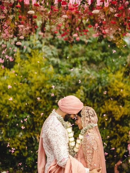 A moment of pure joy under a canopy of pink and white blooms. This garden-style Anand Karaj setup was designed to feel light, airy, and full of love, with petals showering the couple as they took their vows.