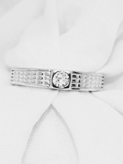 This close-up on a soft background showcases the fine details of the band ring, from the grid-like texture to the secure setting of the solitaire.