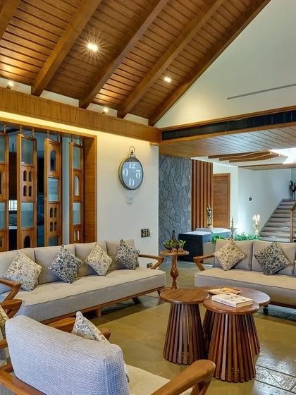 The living room of the 'Anandi' house features a high, pitched wooden ceiling and comfortable, contemporary furniture, creating a spacious yet cozy atmosphere.