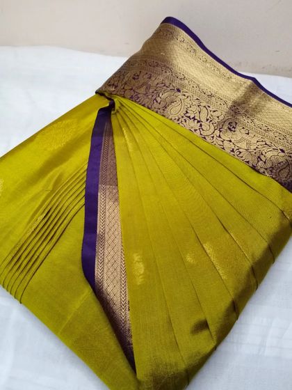 An olive green saree with a rich purple and gold border. It has been pleated and box folded, making it easy to store and travel with.