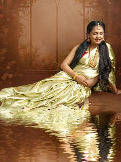An artistic shot with a water reflection effect, showing a mom-to-be in a beautiful green saree in a moment of quiet contemplation.