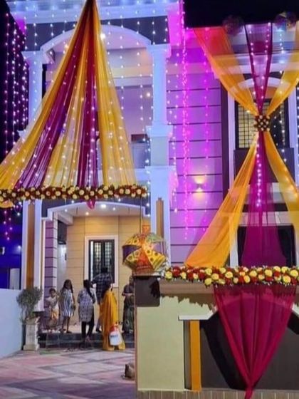 A beautiful night-time decoration for a house entrance, with yellow and pink drapes lit by fairy lights. The decorated umbrella adds a quirky touch.