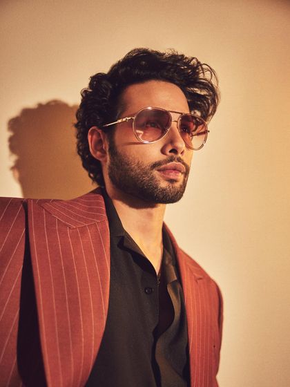 A close-up of Siddhant Chaturvedi in a custom pinstripe suit. The tinted aviator glasses add a cool, retro vibe to the sharp tailoring.