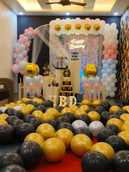 This birthday setup uses a soft pastel pink and blue arch with gold accents. The floor covered in black and gold balloons provides a dramatic contrast, perfect for a memorable celebration.