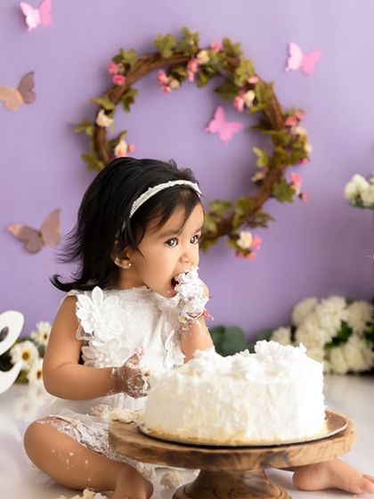This baby girl is getting right into her first birthday cake during a whimsical butterfly-themed session in the studio.