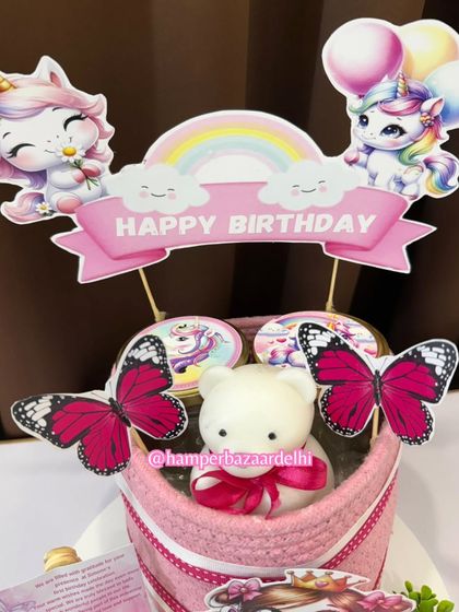 A magical unicorn-themed hamper in a pink cotton jute basket, decorated with butterflies and a cute teddy candle.