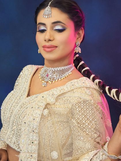 This shot highlights the beautiful, braided hairstyle with pearl details, a perfect complement to the elegant white lehenga and glittery eye makeup.