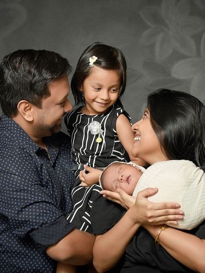 A candid and joyful family portrait with a newborn and older sister. The genuine smiles and loving looks between all four family members make this a truly priceless memory.