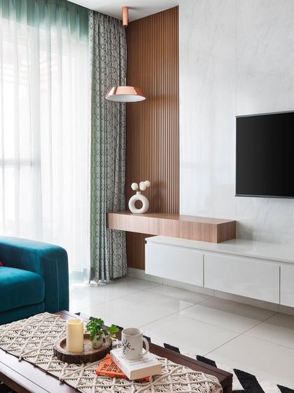 Beauty lies in the details of this TV unit. The design combines a wood-finish fluted panel with a clean white floating console, creating a modern look. A pop of color from the teal sofa and copper pendant light completes the space.