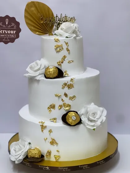 This grand three-tier cake was created for a sangeet party. The pure white design is accented with gold leaf, Ferrero Rocher chocolates, and white roses for a look of pure luxury.