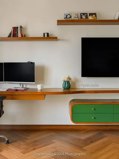 The master bedroom in 'Cover me in Sunshine' includes this integrated study and TV unit. The long wooden desk provides ample workspace, complemented by floating shelves and a curved green storage console.
