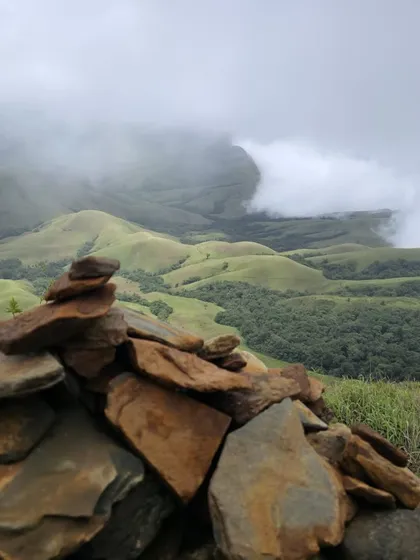 A small stack of balanced stones, or cairn, with the beautiful green valleys of Kudremukha National Park in the background.
