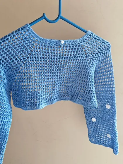 The light blue mesh shrug on a hanger. The cropped design makes it a stylish piece to layer over dresses, tanks, or tops.