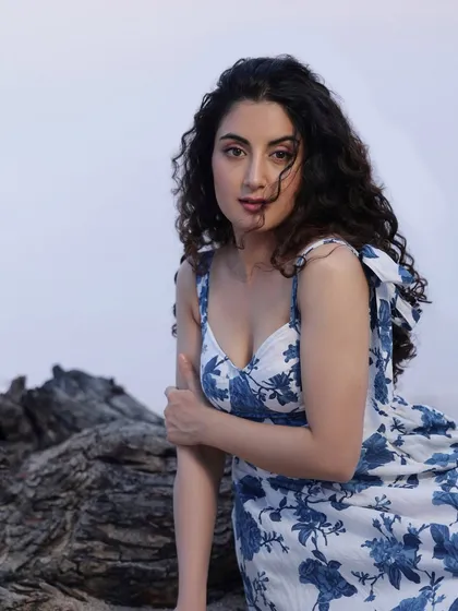 A beautiful outdoor portrait of a woman with curly hair in a blue and white floral dress, posing against a rocky background.