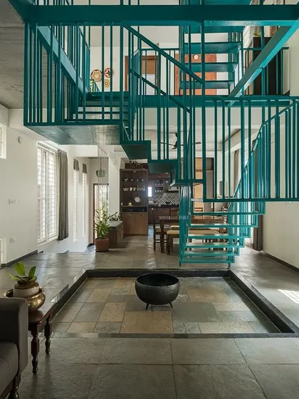 For the 'Jodi Mane' project, the staircase is more than just for circulation; it's the heart of the home. This suspended blue metallic stairway acts as a sculptural element, connecting spaces vertically while maintaining an open, airy feel around the central courtyard.