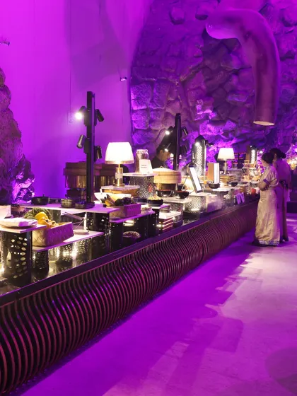 A buffet line illuminated by dramatic purple lighting, set against a unique, cave-like wall texture. We believe the food display should be as captivating as the venue itself.