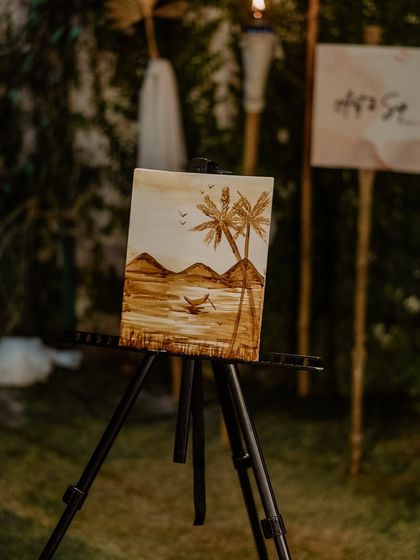 A finished coffee painting of a serene beach scene, displayed on a mini easel. It’s amazing what you can create with just coffee.