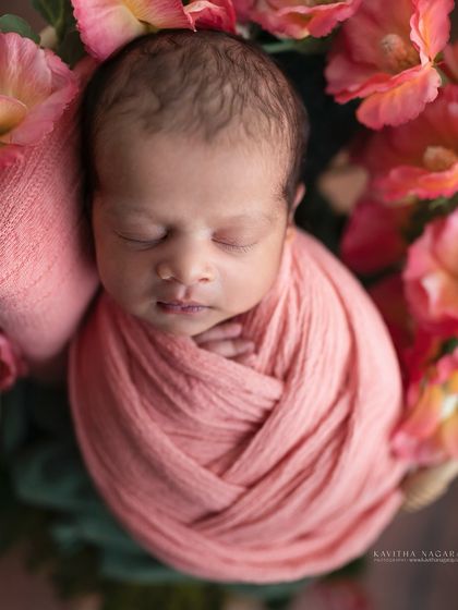A newborn wrapped in a soft pink swaddle, nestled amongst vibrant flowers. The rich colors and textures create a warm, artistic portrait that feels like a dream.