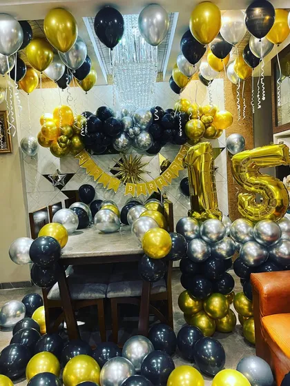 A lavish 15th birthday party decoration at home. The room is filled with black, gold, and silver balloons, creating a festive and glamorous atmosphere.