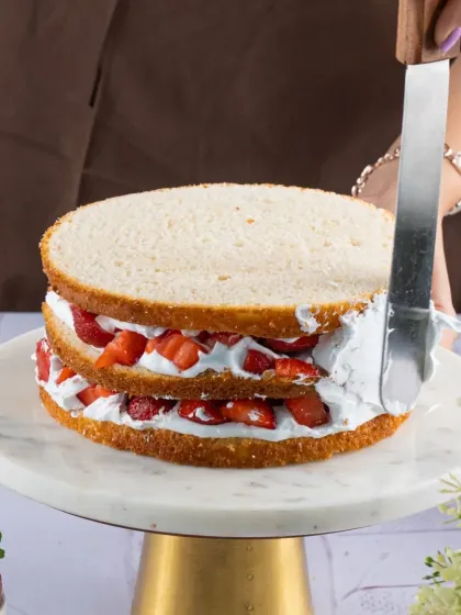 Assembling our Strawberry Almond Gateau. You can see the layers of light sponge cake, fresh cream, and plenty of chopped strawberries.
