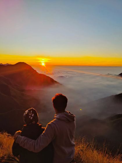 A romantic shot of a couple watching the sunrise over the clouds in Munnar, perfect for my honeymoon packages.