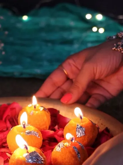 A hand arranging my glowing Laddoo candles in a traditional brass thali with rose petals, creating a stunning festive centerpiece.