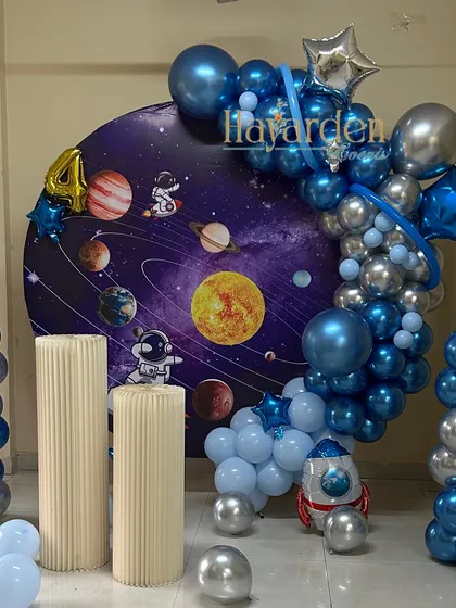 An out-of-this-world space theme for a 4th birthday. This features a galaxy backdrop, a silver and blue balloon garland, and astronaut cutouts.