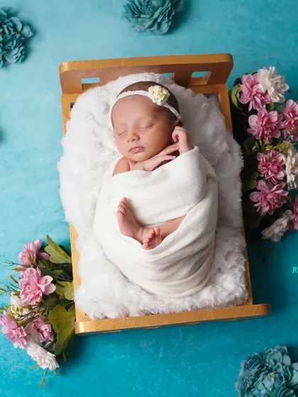 A beautifully swaddled newborn in a tiny bed, surrounded by flowers. This overhead shot showcases the symmetry and artistry of our posing.