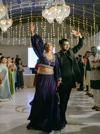 A full-length shot of the couple's energetic entrance at their Sangeet celebration, with guests cheering them on.