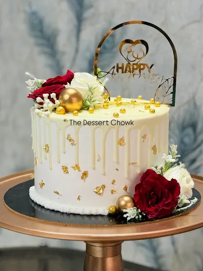 An elegant white drip cake decorated with red and white roses and gold leaf flakes. This tall cake is perfect for an anniversary or a special birthday.