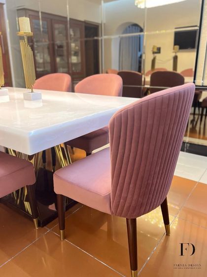 An elegant dining set featuring a white onyx table and chairs upholstered in a pleated pink velvet. The gold-finished table base and chair legs add a touch of warmth and glamour.