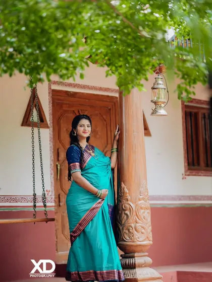 A graceful solo shot of the expectant mother in a vibrant teal saree, posing by a traditional swing.