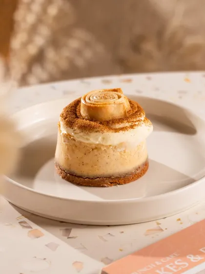 A mini cinnamon roll cheesecake. The warm colors and familiar swirl on top evoke a sense of comfort and nostalgia.