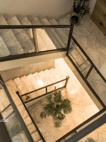 An overhead view of a square staircase with glass railings, looking down into a well-lit atrium.
