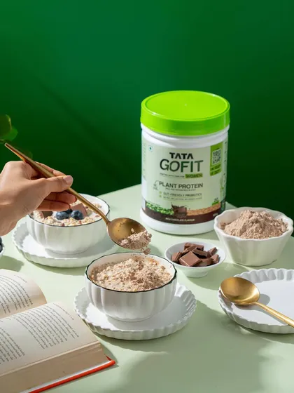 This lifestyle shot captures the action of adding protein powder to a breakfast bowl, making the product feel like a natural and easy addition to a healthy meal.