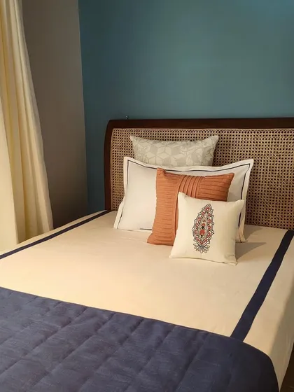 A bedroom in the Alibaug villa where I paired a cane headboard with a deep blue wall. The look is completed with custom bedding and a mix of embroidered and textured cushions for a coastal, serene feel.