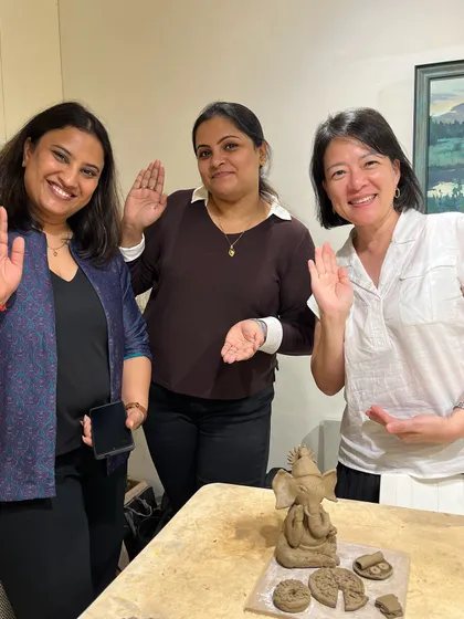 Three participants happily wave after completing their Ganesha idols in a clay sculpting session. A perfect example of a fun and festive workshop.