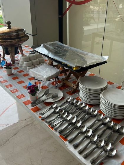 A clean and organized serving station at the Kotak Mahindra Bank Dussehra lunch, with stacks of plates and cutlery ready for guests.