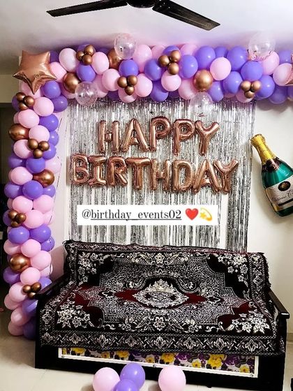 A living room corner transformed with a balloon arch, silver fringe curtain, and a champagne foil balloon for a festive home party.