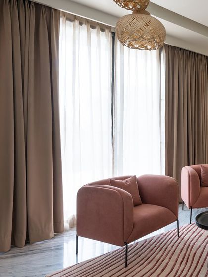 A detail shot of the living room, focusing on the dusty pink armchairs and layered curtains. This composition highlights our use of color and texture to create inviting seating areas.