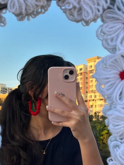 A mirror selfie showing off my red and green hoop earrings. These are made by wrapping crochet around a hoop for a bold, festive look.