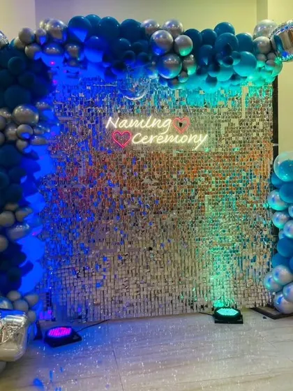 The sequin wall backdrop for the naming ceremony, shown here with a mix of blue and green lighting. The silver and blue balloon frame completes the modern look.