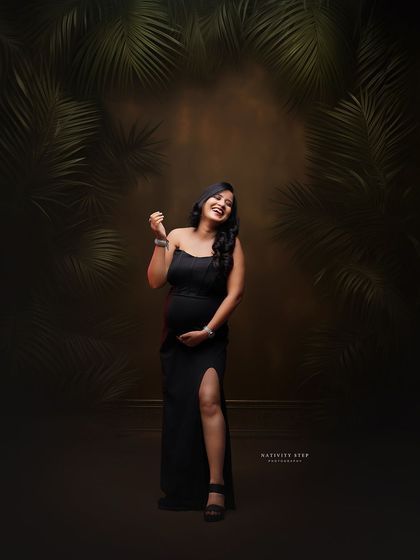 A joyful solo portrait in a classic black gown. The tropical leaf backdrop adds a touch of modern style to this studio shot.