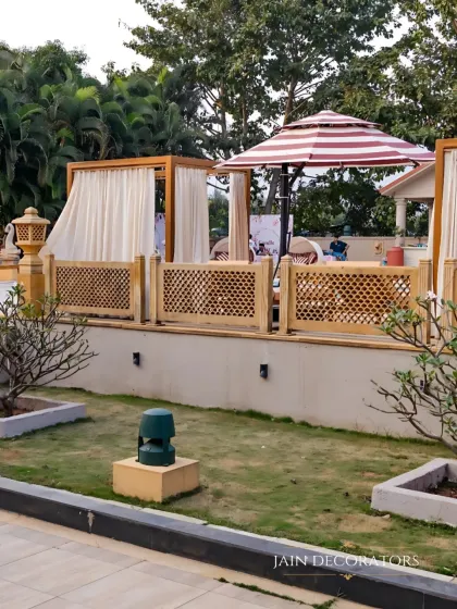 A serene outdoor lounge area. I used wooden cabanas with white drapes and traditional jali screens to create a comfortable and stylish space for guests to relax.