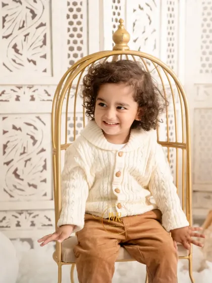 A candid shot of a toddler boy looking away with a sweet smile, seated in a golden prop chair.