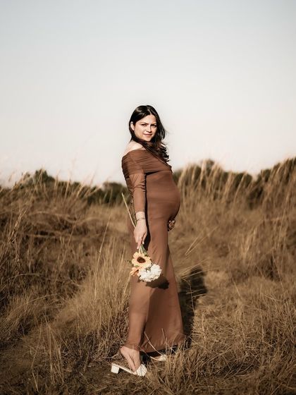 A classic solo maternity portrait in a field of tall grass. The mom-to-be holds a bouquet and looks at the camera with a calm and confident gaze.